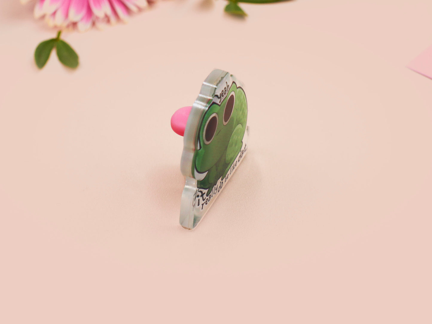 Clear acrylic pin badge with a pink heart-shaped rubber pin back clasp. The design of the pin badge is a cute cartoon stressed frog with the quote yeah it really do be like dat.