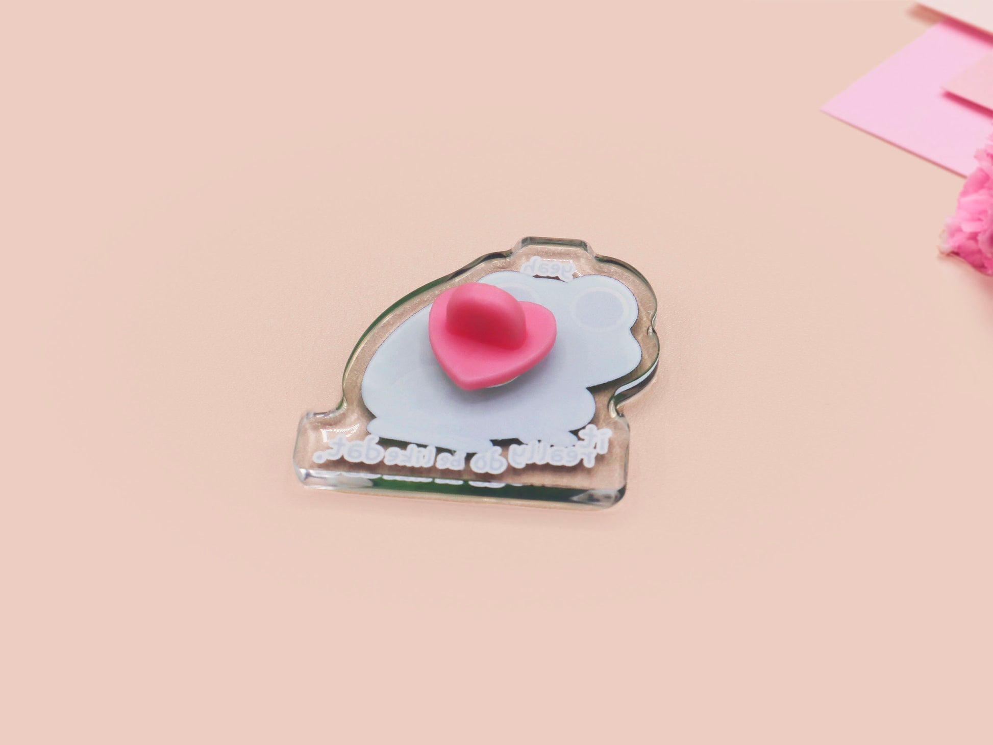 Clear acrylic pin badge with a pink heart-shaped rubber pin back clasp. The design of the pin badge is a cute cartoon stressed frog with the quote yeah it really do be like dat.