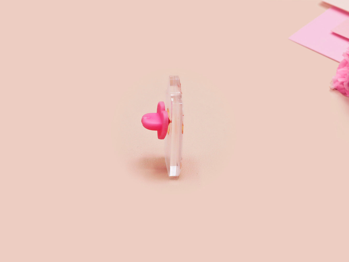 A clear acrylic pin badge with a pink heart-shaped pin back clasp. The design of the pin badge is of a cute chibi goose wearing a paper hat with the quote you silly goose.