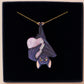Mixed material handmade necklace of chibi cartoon bat hanging upside down holding a pearlescent Ouija planchette, with a gold chain and black gift box.