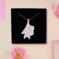 Back of mixed material handmade necklace of chibi cartoon bat hanging upside down holding a pearlescent Ouija planchette, with a gold chain and black gift box.