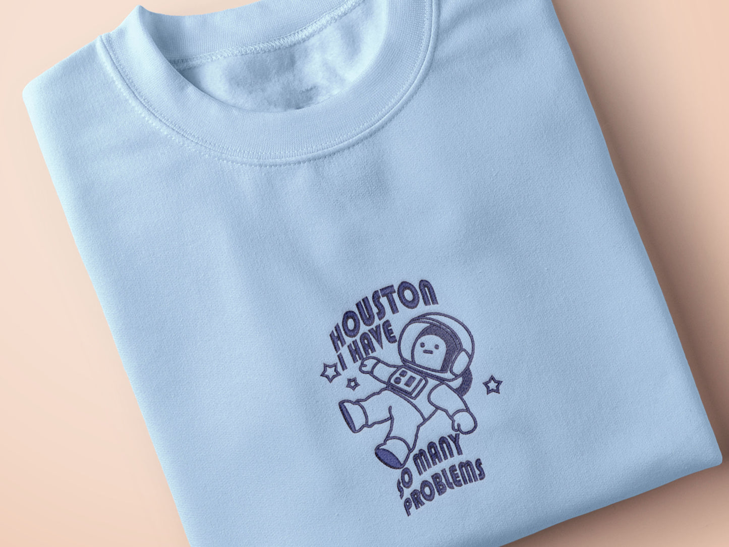 T-shirt with an embroidered blue design of a cute chibi astronaut surrounded by the funny quote Houston I have so many problems