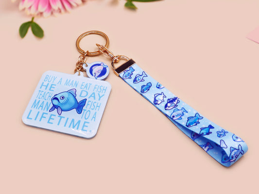 Acrylic epoxy underwater fish keychain with a large acrylic charm of a blue fish with the quote buy a man eat fish he day teach fish man to a lifetime, a smaller charm of a cute fish and a matching underwater lanyard.