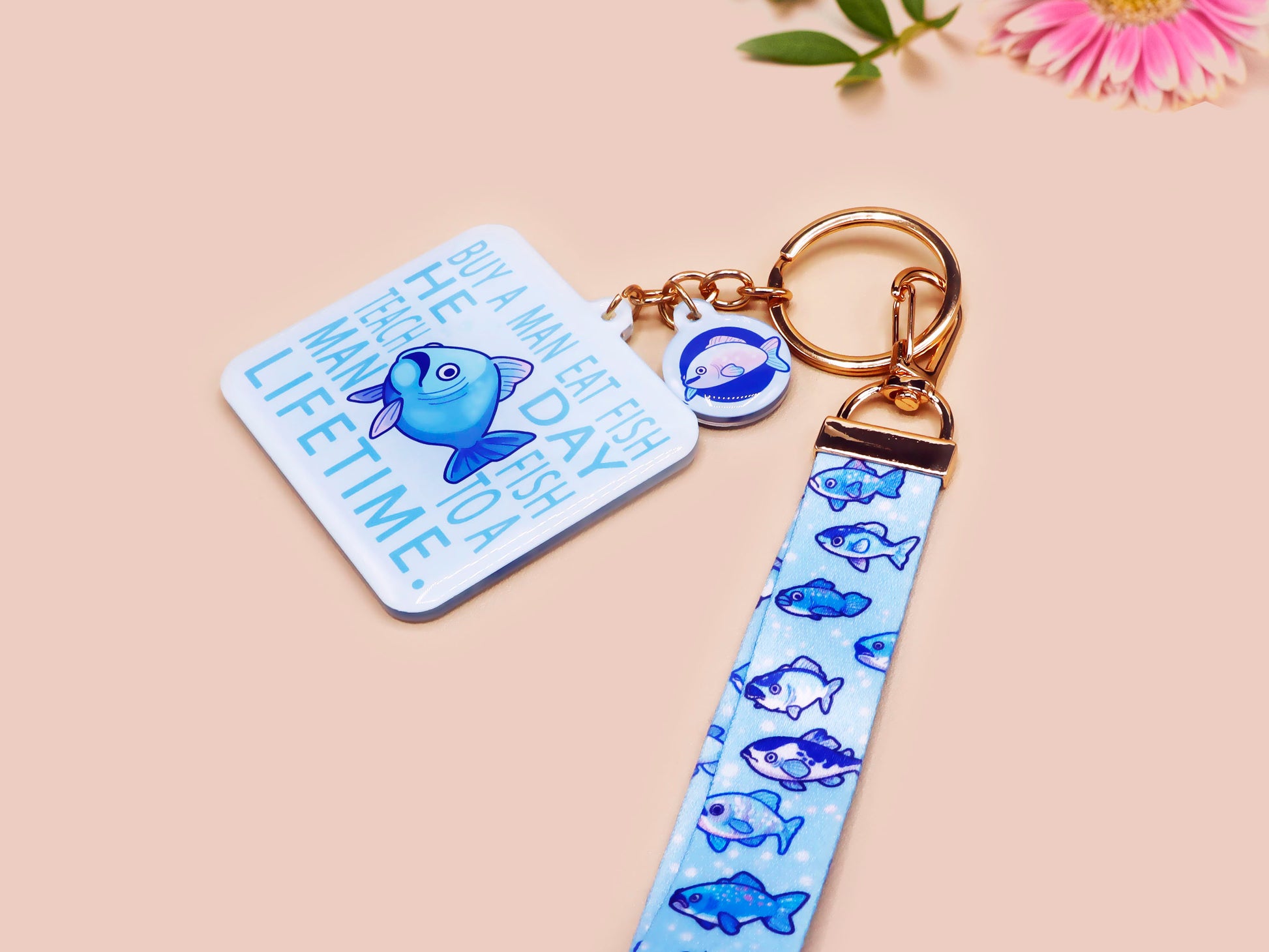 Acrylic epoxy underwater fish keychain with a large acrylic charm of a blue fish with the quote buy a man eat fish he day teach fish man to a lifetime, a smaller charm of a cute fish and a matching underwater lanyard.