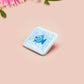 A clear acrylic pin badge with a pink heart-shaped pin back clasp. The design of the pin badge is of a cute chibi blue fish with the quote buy a man eat fish he day teach fish man to a lifetime.