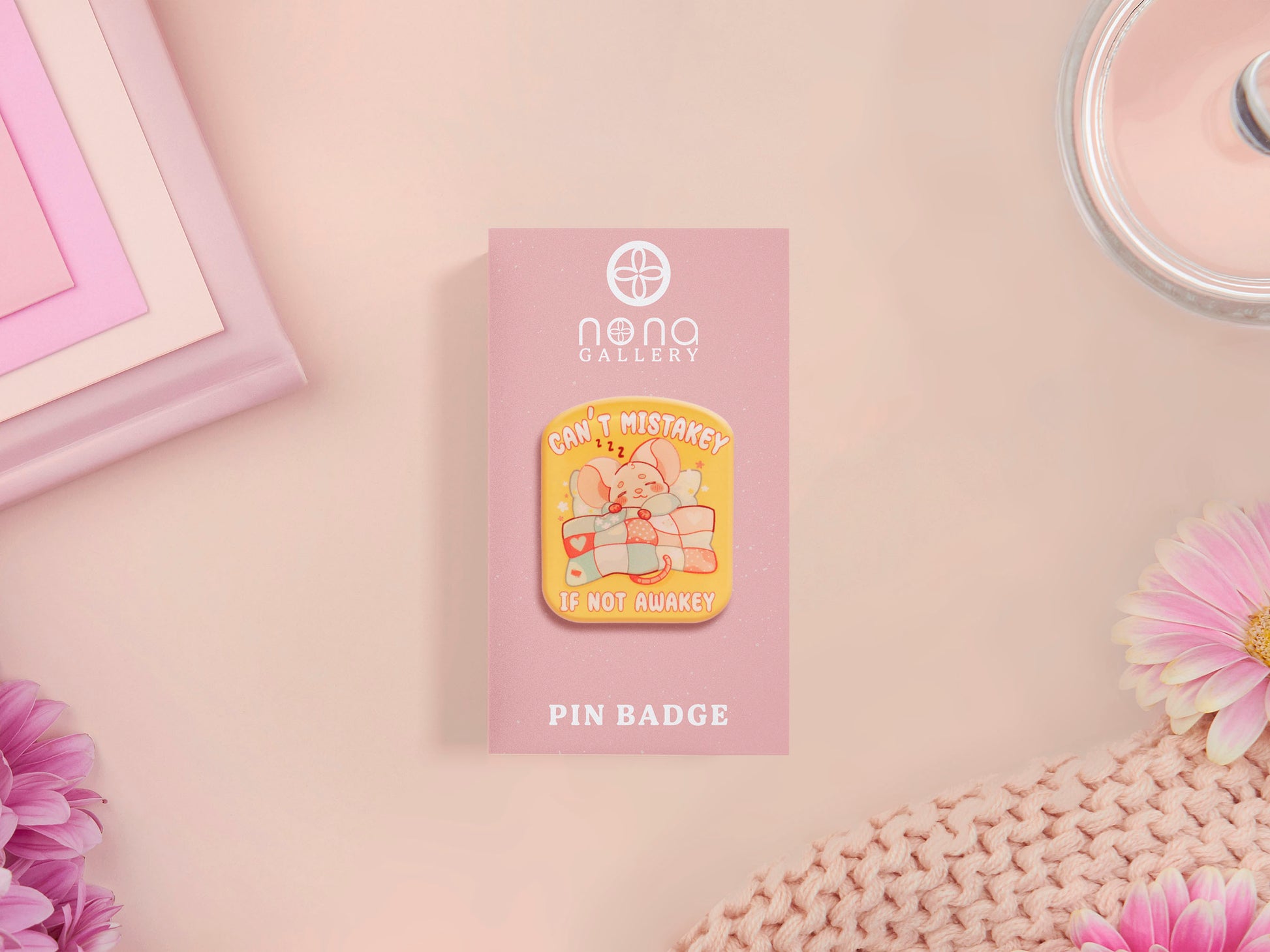 A yellow acrylic pin badge with a pink heart-shaped pin back clasp. The design of the pin badge is of a cute mouse napping in bed with a patchwork quilt with the quote can't mistakey if not awakey.
