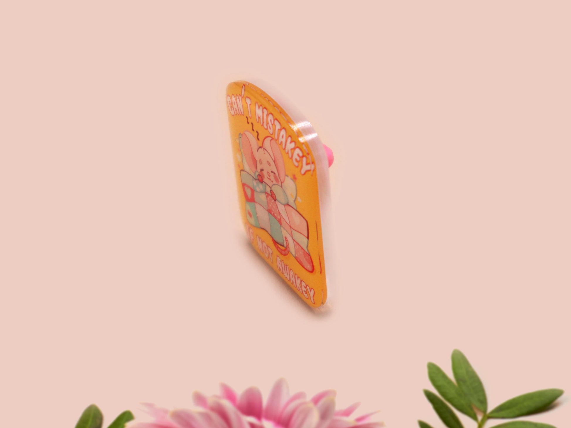A yellow acrylic pin badge with a pink heart-shaped pin back clasp. The design of the pin badge is of a cute mouse napping in bed with a patchwork quilt with the quote can't mistakey if not awakey.