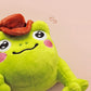 An adorable green frog plushie toy with cute embroidered eyes and facial expression, wearing a cowboy hat with a brown ribbon, and a hang tag describing the frog as Carl.
