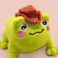 An adorable green frog plushie toy with cute embroidered eyes and facial expression, wearing a cowboy hat with a brown ribbon, and a hang tag describing the frog as Carl.