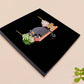 Mixed material handmade necklace of chibi cartoon cat sat on a witch's book shelf with pearlescent crystal. knocking a plant pot of the edge, with a gold chain and black gift box.