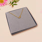 A gold lobster fastener on a gold chain necklace in a grey velvet gift box