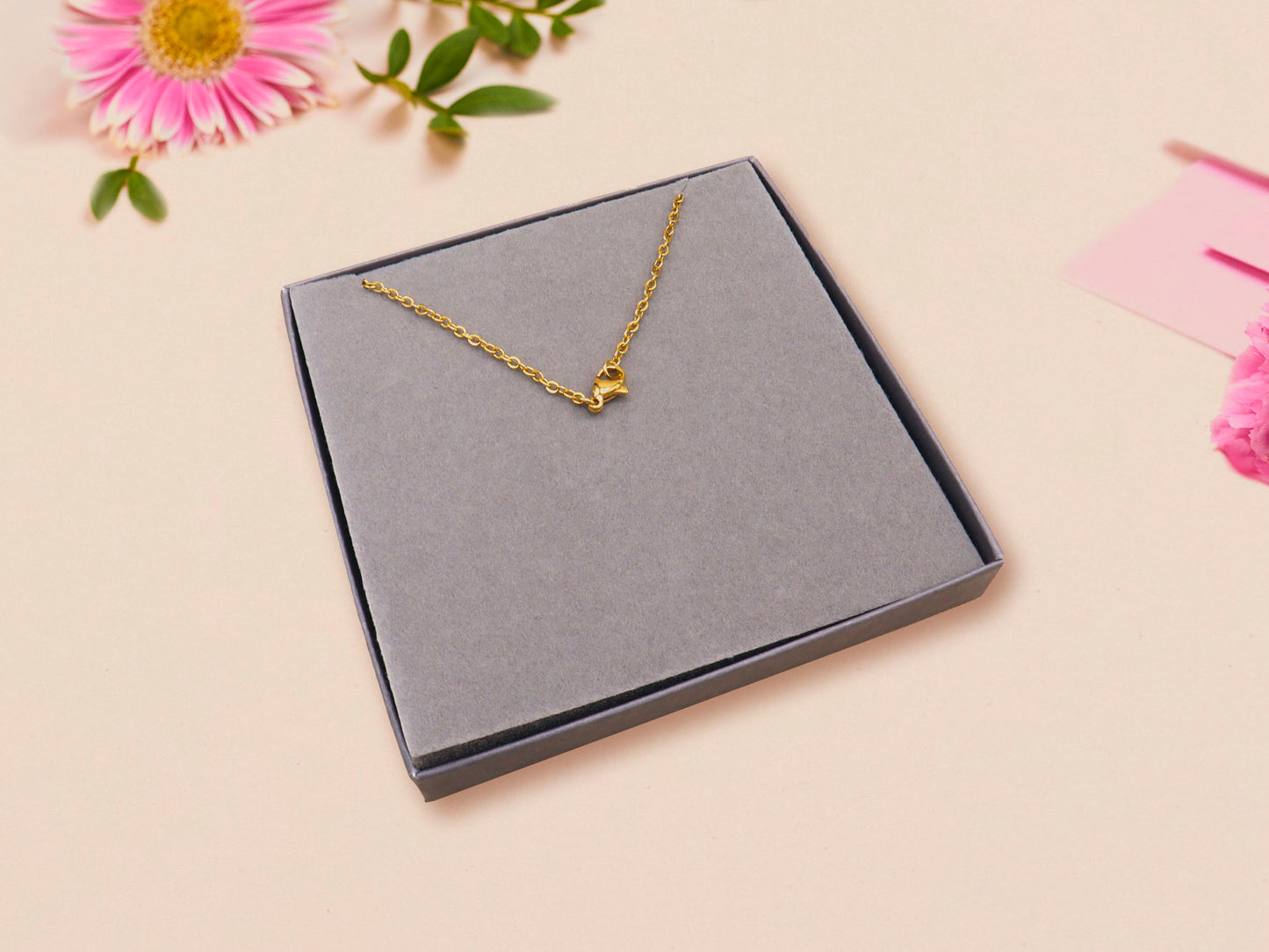 A gold lobster fastener on a gold chain necklace in a grey velvet gift box