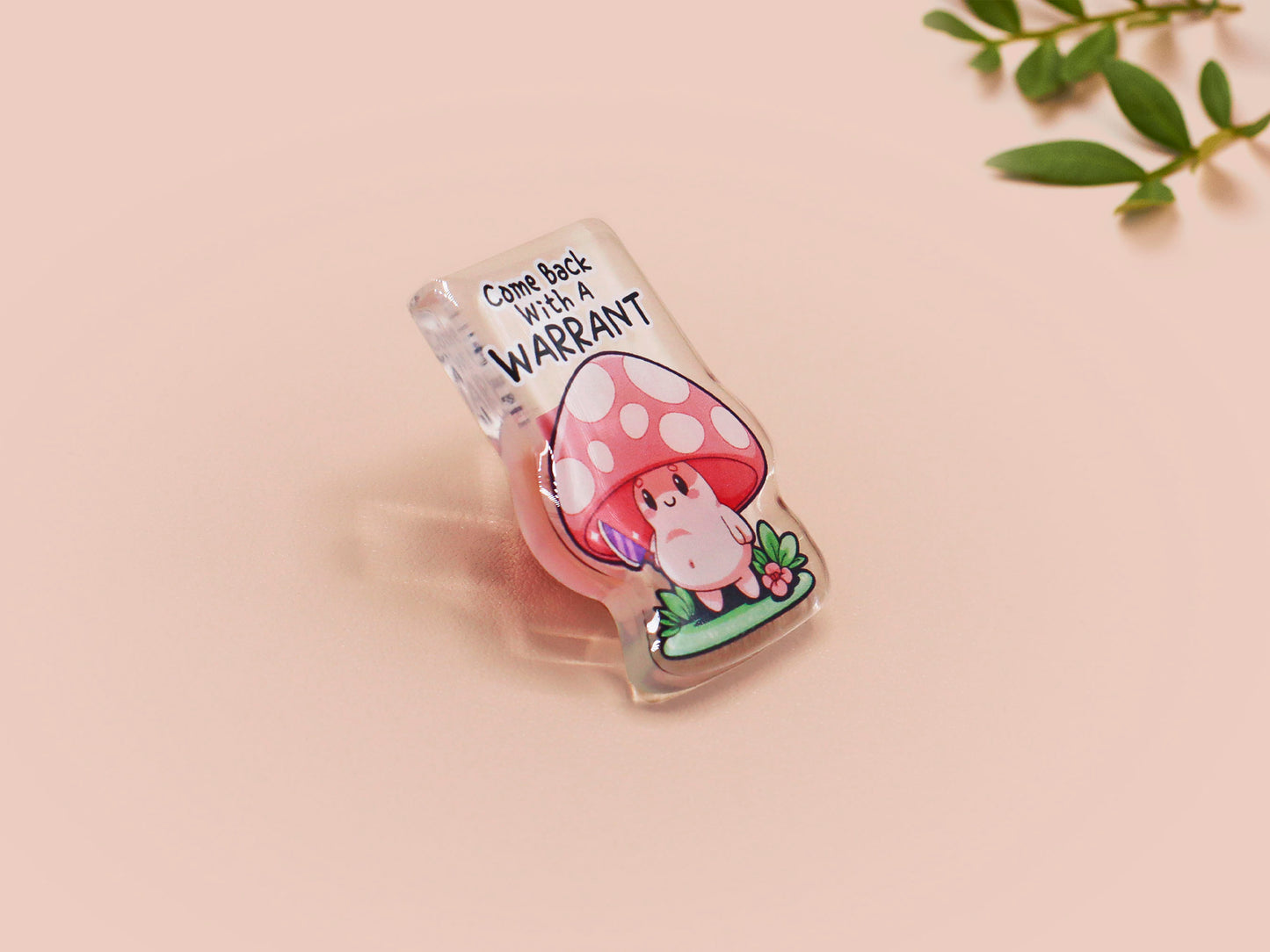 This cute transparent acrylic pin badge has a pink rubber heart shrimp pin-back clasp. The design is of a chibi cartoon mushroom with the text "Come back with a warrant."