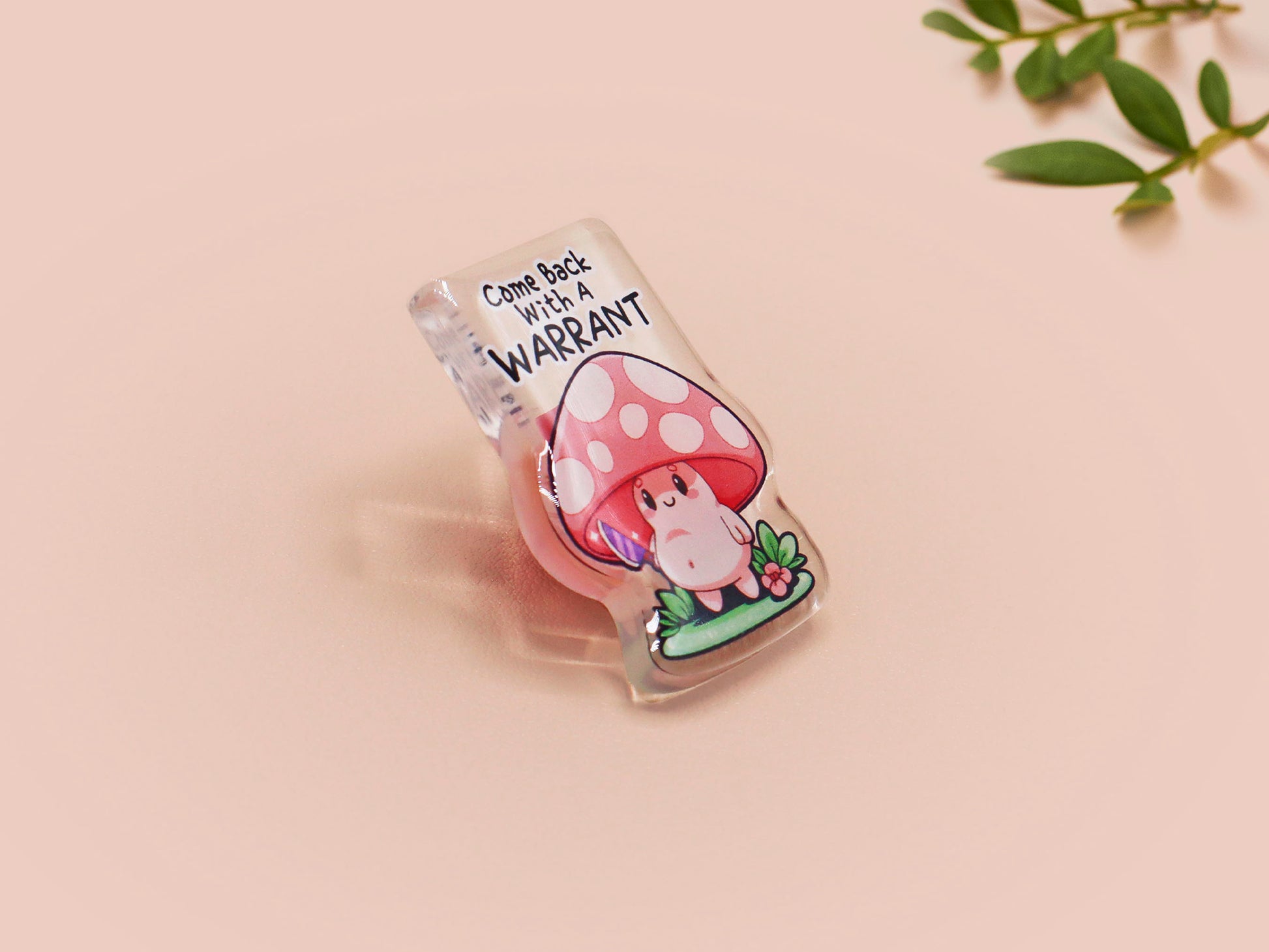 This cute transparent acrylic pin badge has a pink rubber heart shrimp pin-back clasp. The design is of a chibi cartoon mushroom with the text "Come back with a warrant."