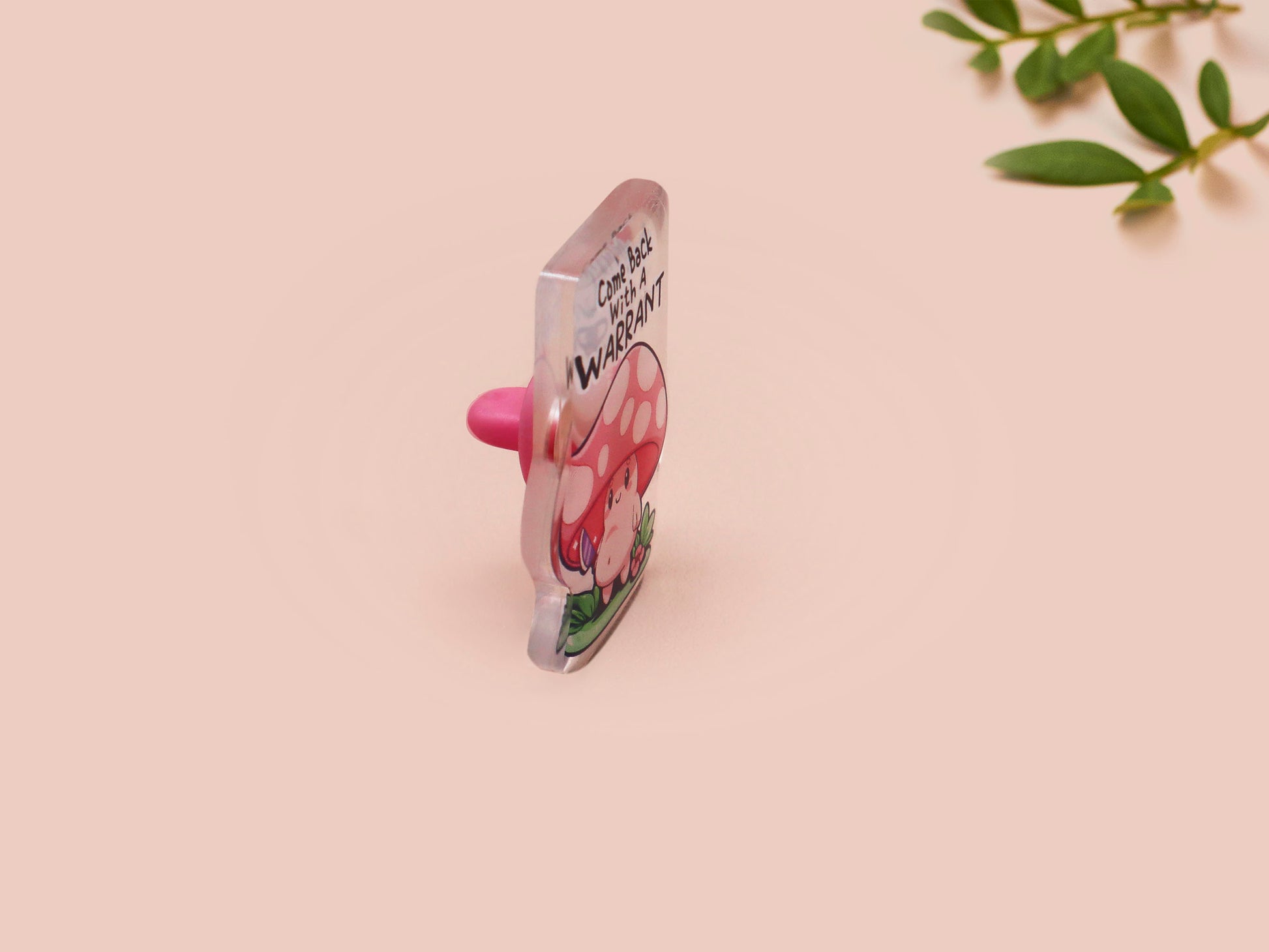 This cute transparent acrylic pin badge has a pink rubber heart shrimp pin-back clasp. The design is of a chibi cartoon mushroom with the text "Come back with a warrant."