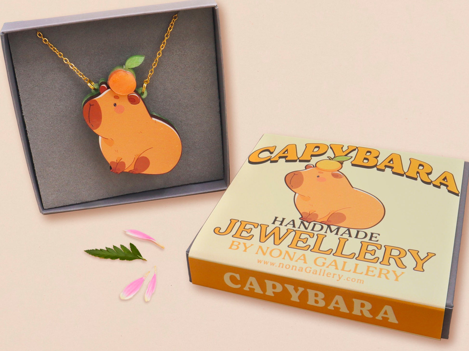 Adorable cute capybara with an orange on its head necklace made of wood and glitter pearlescent acrylic with a gold chain, displayed in a velvet gift box with a unique cute capybara sleeve design.