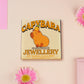 Adorable cute capybara with an orange on its head necklace made of wood and glitter pearlescent acrylic with a gold chain, displayed in a velvet gift box with a unique cute capybara sleeve design.