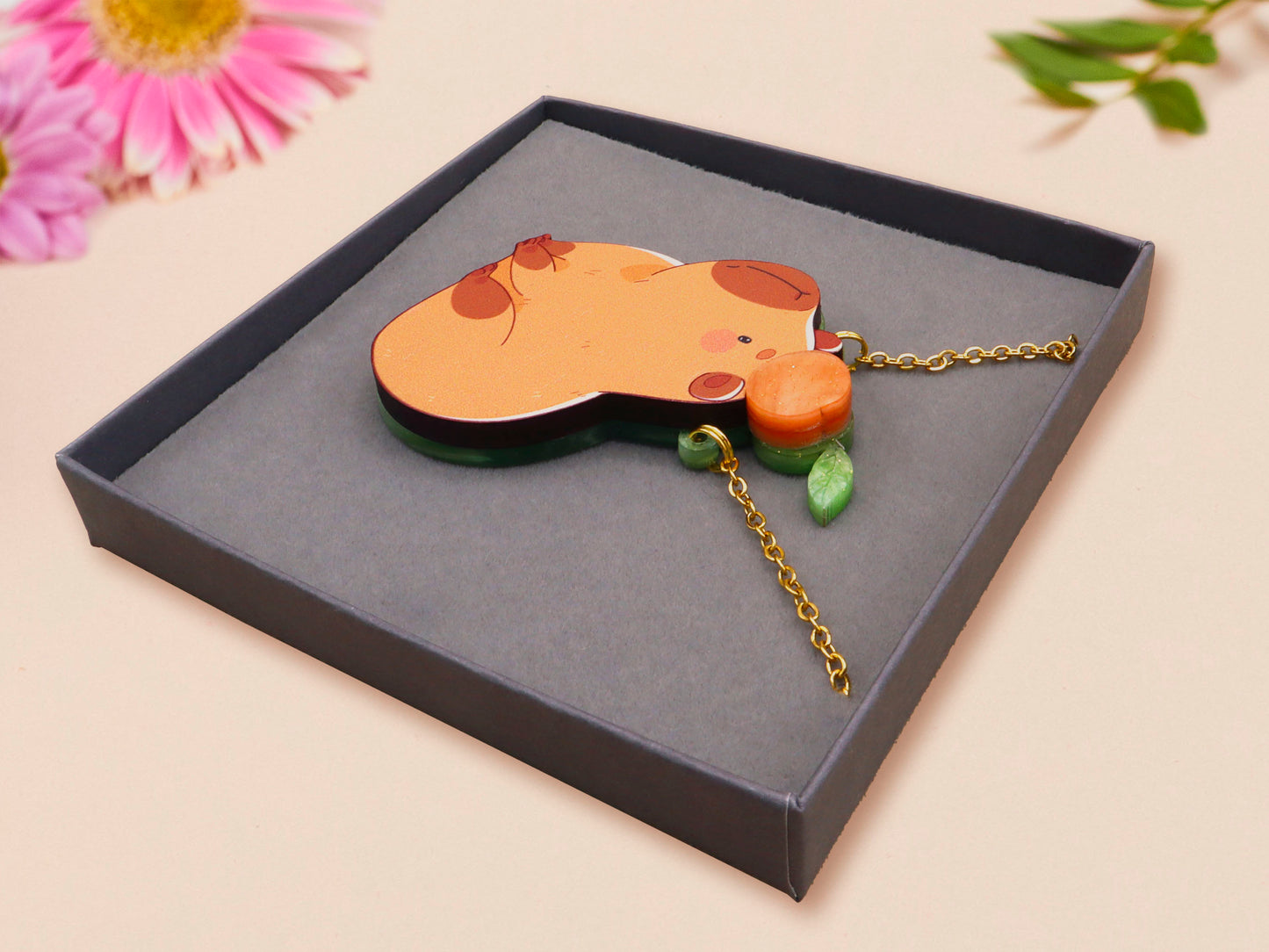 Adorable cute capybara with an orange on its head necklace made of wood and glitter pearlescent acrylic with a gold chain, displayed in a velvet gift box with a unique cute capybara sleeve design.