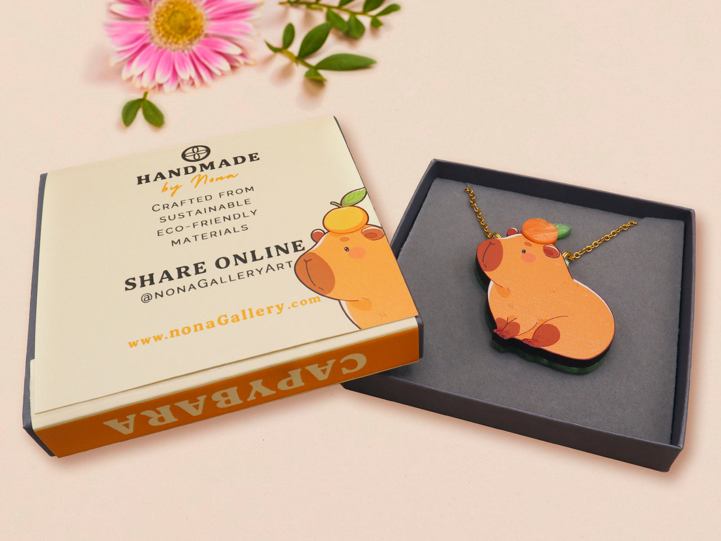 Adorable cute capybara with an orange on its head necklace made of wood and glitter pearlescent acrylic with a gold chain, displayed in a velvet gift box with a unique cute capybara sleeve design.