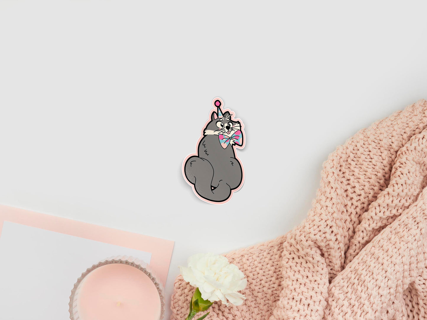 Large sticker of digital illustration cartoon of a cute grey cat with it's tongue cheekily pocking out its mouth, in a blue and pink spotted party hat and bow tie