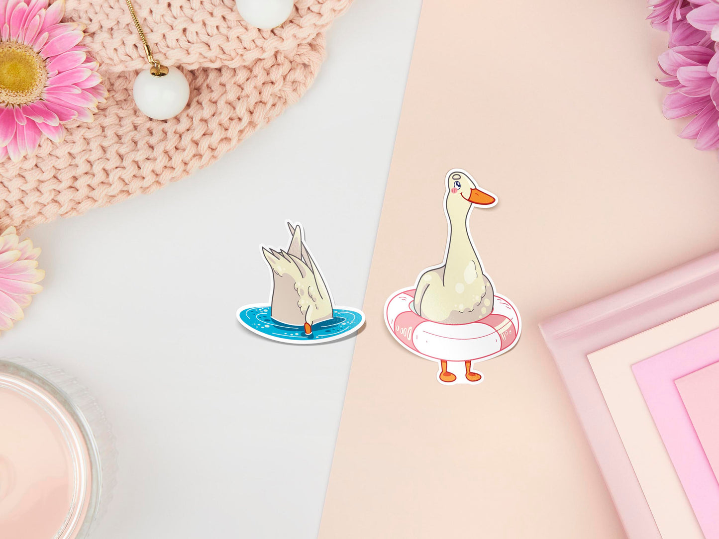 Two stickers of digitally illustrated cartoon of white ducks, one upside down in the water and you can only see it's bum, the other is wearing a safety flotation ring