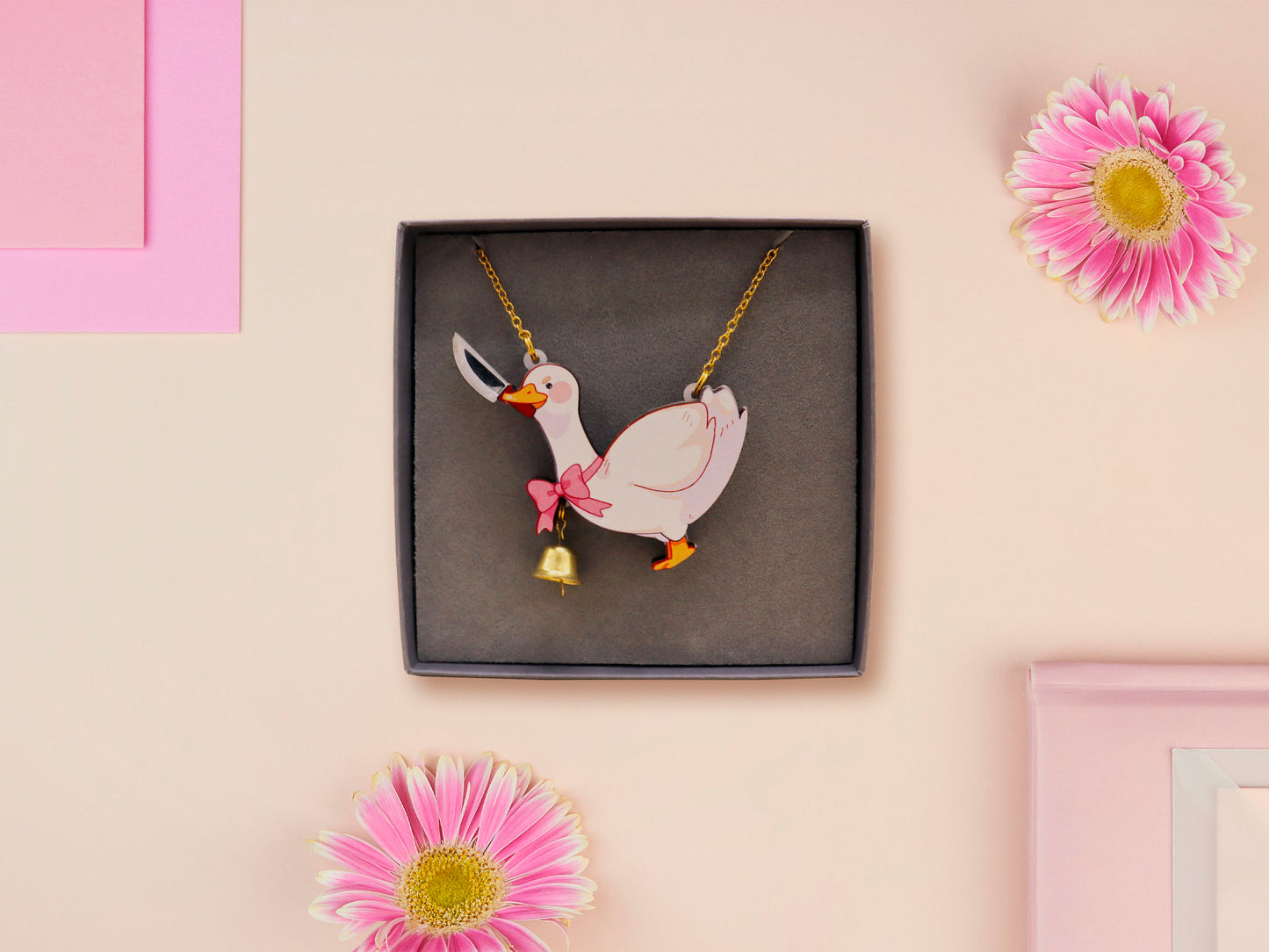 An adorable cute goose with a bell and pink bow necklace made of wood and glitter pearlescent acrylic with a gold chain is displayed in a velvet gift box with a unique cute goose sleeve design.