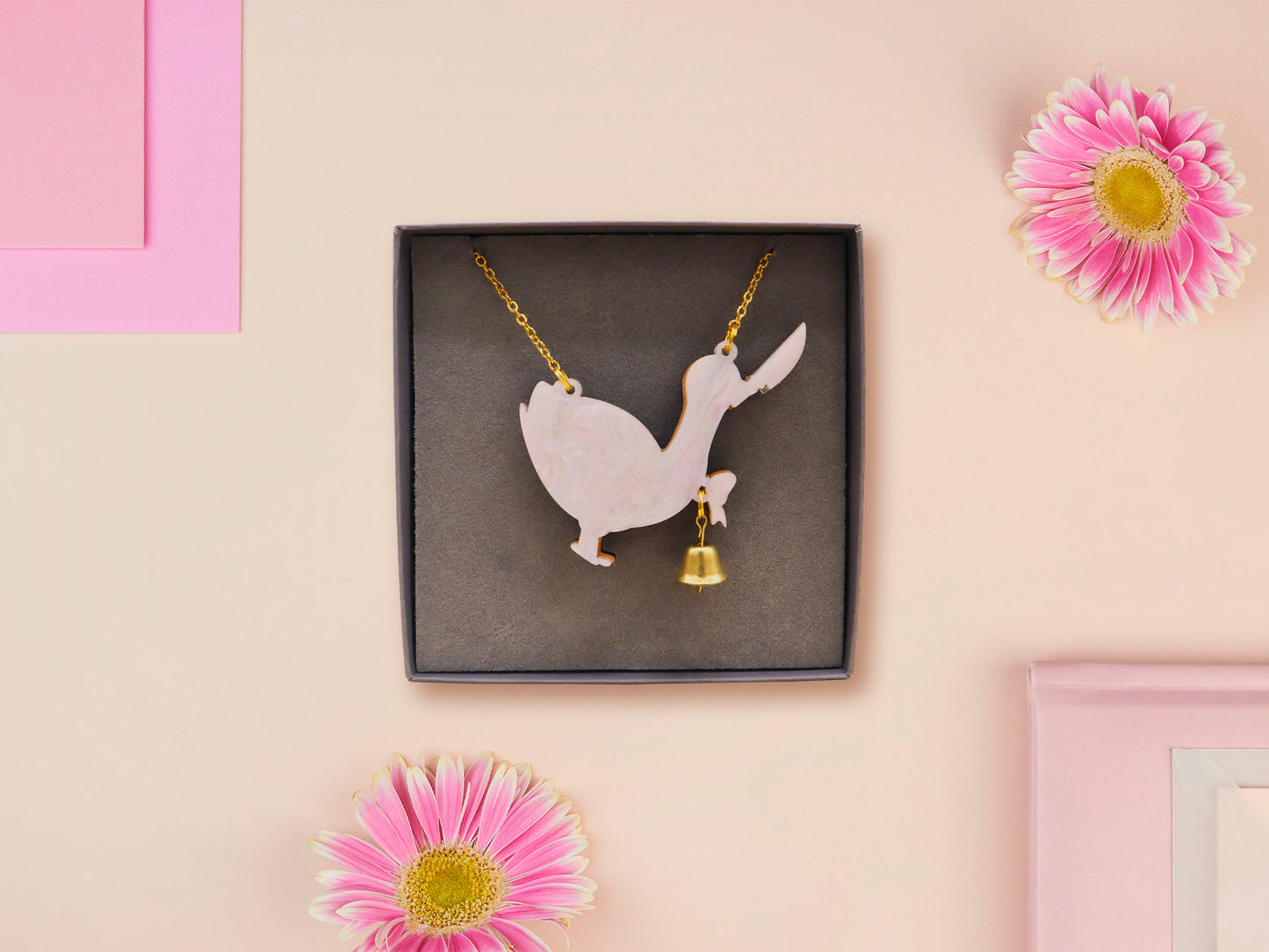 An adorable cute goose with a bell and pink bow necklace made of wood and glitter pearlescent acrylic with a gold chain is displayed in a velvet gift box with a unique cute goose sleeve design.