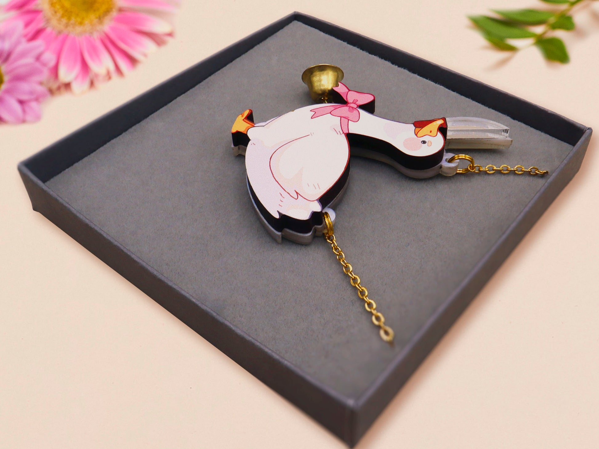 An adorable cute goose with a bell and pink bow necklace made of wood and glitter pearlescent acrylic with a gold chain is displayed in a velvet gift box with a unique cute goose sleeve design.