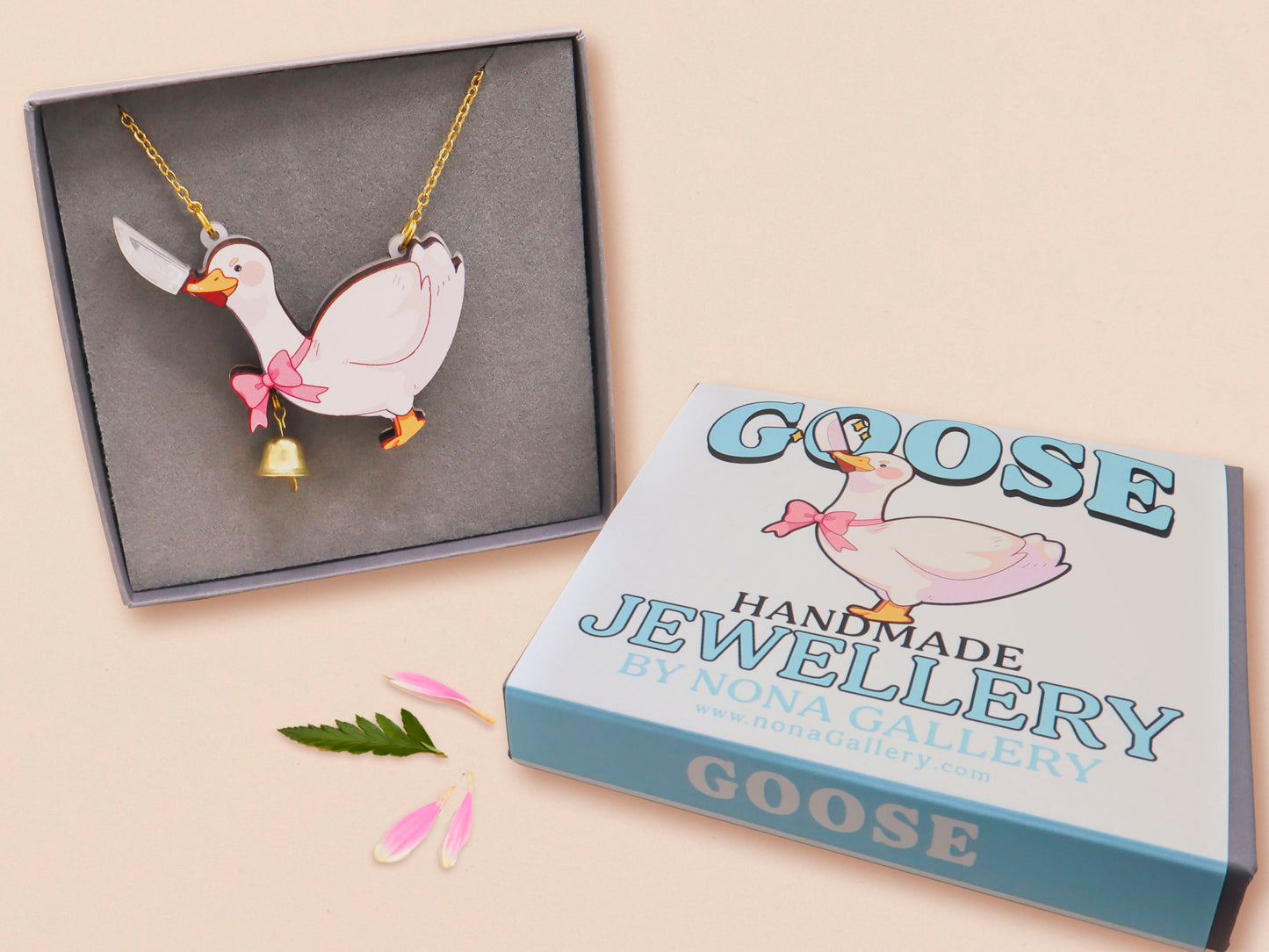 An adorable cute goose with a bell and pink bow necklace made of wood and glitter pearlescent acrylic with a gold chain is displayed in a velvet gift box with a unique cute goose sleeve design.