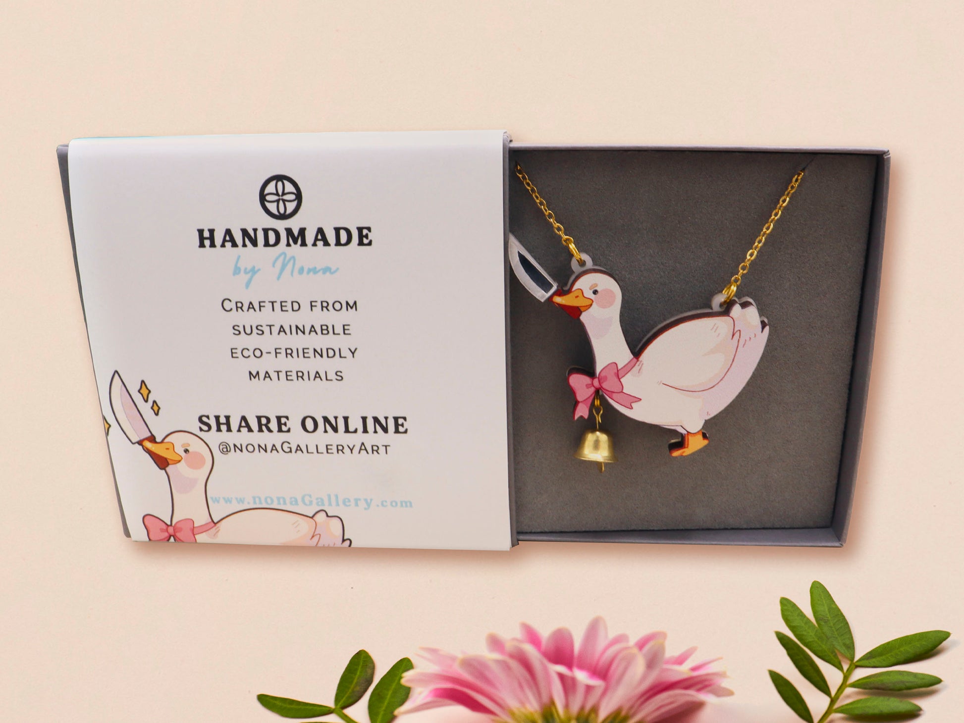 An adorable cute goose with a bell and pink bow necklace made of wood and glitter pearlescent acrylic with a gold chain is displayed in a velvet gift box with a unique cute goose sleeve design.