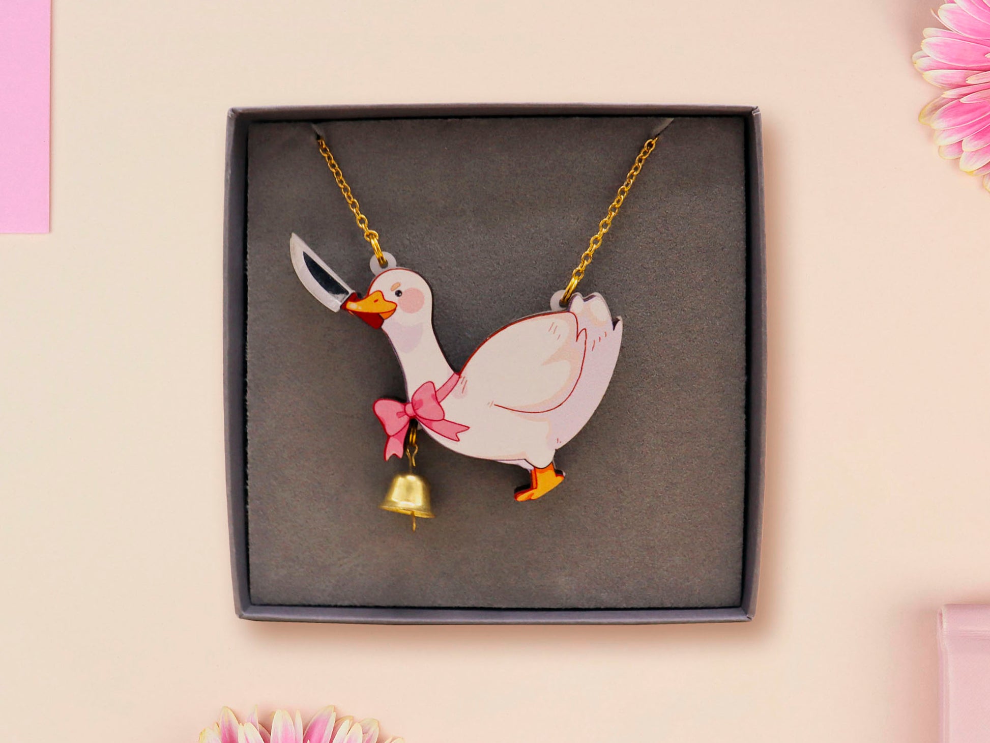 An adorable cute goose with a bell and pink bow necklace made of wood and glitter pearlescent acrylic with a gold chain is displayed in a velvet gift box with a unique cute goose sleeve design.