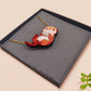 An adorable cute otter holding a clam seashell with a pearl inside necklace made of wood and glitter pearlescent acrylic with a gold chain is displayed in a velvet gift box with a unique cute otter sleeve design.