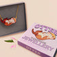 An adorable cute otter holding a clam seashell with a pearl inside necklace made of wood and glitter pearlescent acrylic with a gold chain is displayed in a velvet gift box with a unique cute otter sleeve design.