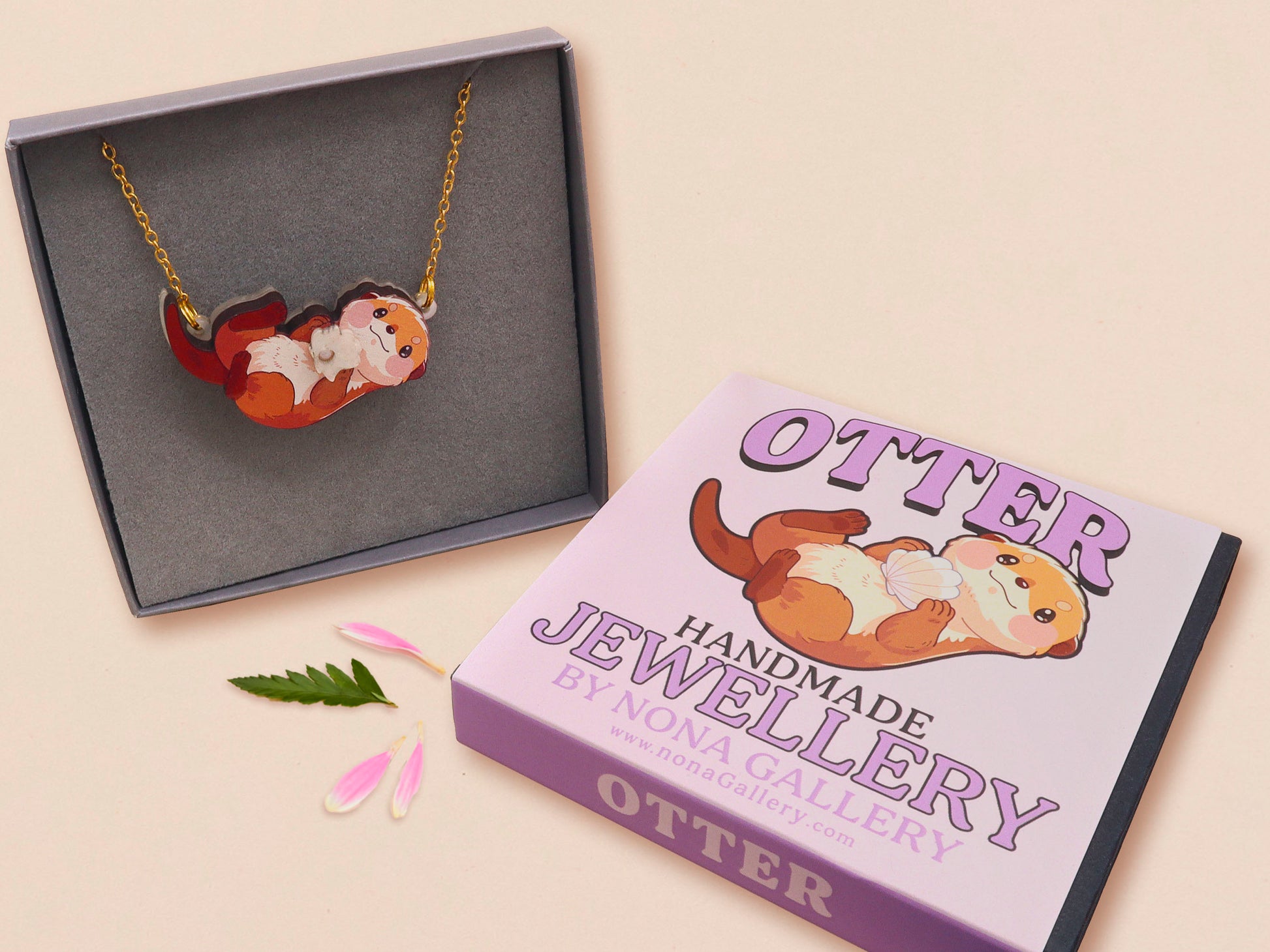 An adorable cute otter holding a clam seashell with a pearl inside necklace made of wood and glitter pearlescent acrylic with a gold chain is displayed in a velvet gift box with a unique cute otter sleeve design.