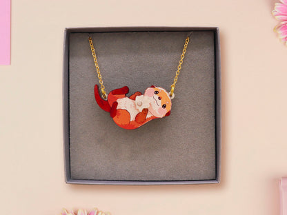 An adorable cute otter holding a clam seashell with a pearl inside necklace made of wood and glitter pearlescent acrylic with a gold chain is displayed in a velvet gift box with a unique cute otter sleeve design.