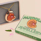 An adorable shy pangolin aardvark holding a heart necklace made of wood and glitter mirror acrylic with a gold chain is displayed in a velvet gift box with a unique cute Pangolin sleeve design.