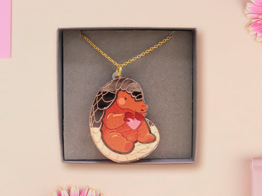 An adorable shy pangolin aardvark holding a heart necklace made of wood and glitter mirror acrylic with a gold chain is displayed in a velvet gift box with a unique cute Pangolin sleeve design.