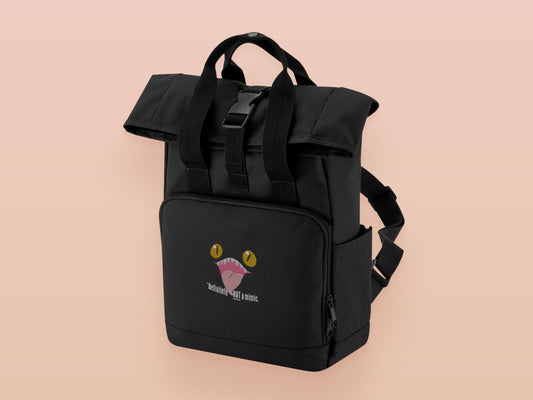 Black roll top backpack with a front pocket and an embroided mimic chest face cryptid design with the text *definetley not a mimic