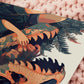 A square art print depicting a young girl with a large trex dinosaur skull fossil over her head surrounded by plants and foliage.