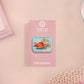 A clear acrylic pin badge with a pink heart-shaped pin back clasp. The design of the pin badge is of a cute relaxing capybara in water with a face mask with the quote don't worry be cappy.