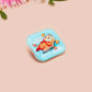 A clear acrylic pin badge with a pink heart-shaped pin back clasp. The design of the pin badge is of a cute relaxing capybara in water with a face mask with the quote don't worry be cappy.