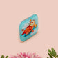 A clear acrylic pin badge with a pink heart-shaped pin back clasp. The design of the pin badge is of a cute relaxing capybara in water with a face mask with the quote don't worry be cappy.