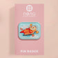 A clear acrylic pin badge with a pink heart-shaped pin back clasp. The design of the pin badge is of a cute relaxing capybara in water with a face mask with the quote don't worry be cappy.
