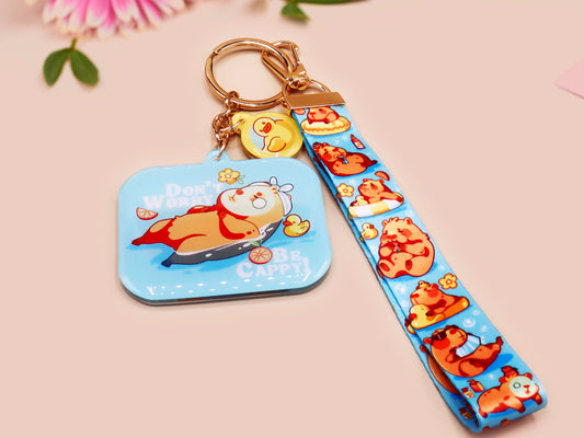 Acrylic epoxy blue capybara spa keychain with a large acrylic charm of a capybara floating in water relaxing with a face mask with the quote don't worry be cappy, a smaller charm of a cute rubber duck and a matching capybara spa day lanyard.