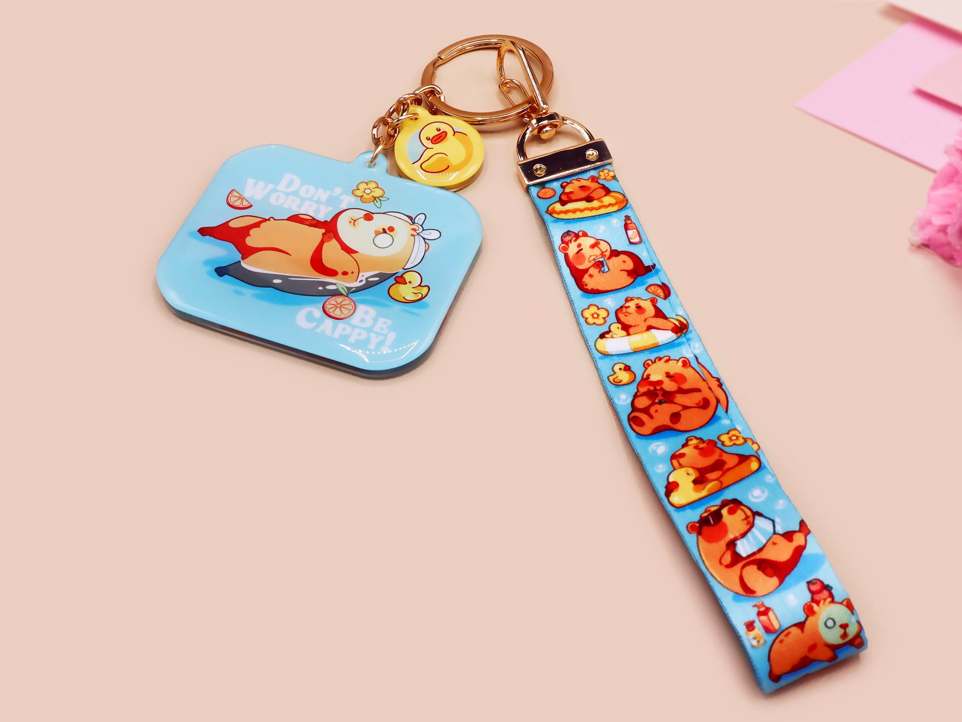Acrylic epoxy blue capybara spa keychain with a large acrylic charm of a capybara floating in water relaxing with a face mask with the quote don't worry be cappy, a smaller charm of a cute rubber duck and a matching capybara spa day lanyard.