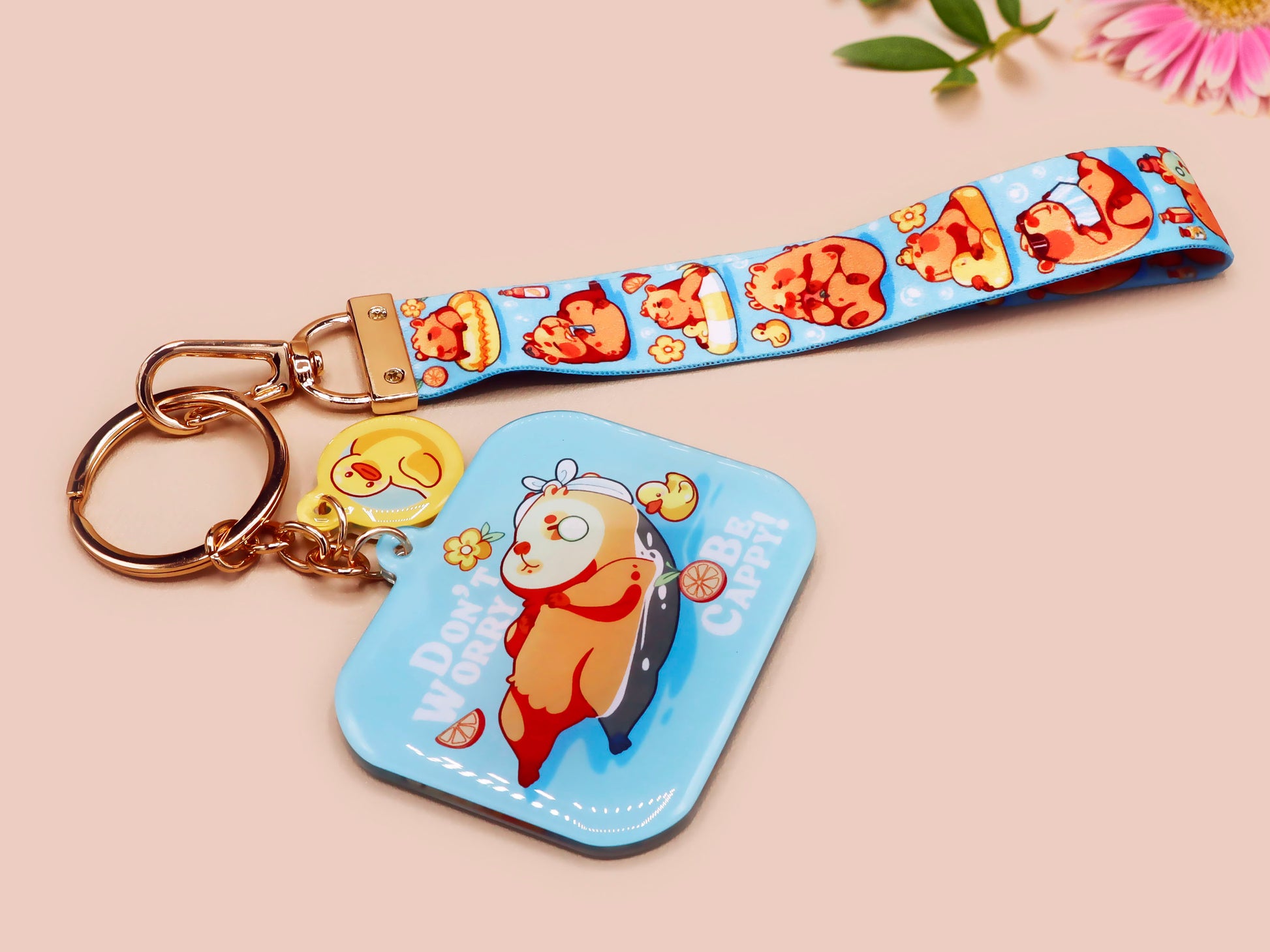 Acrylic epoxy blue capybara spa keychain with a large acrylic charm of a capybara floating in water relaxing with a face mask with the quote don't worry be cappy, a smaller charm of a cute rubber duck and a matching capybara spa day lanyard.