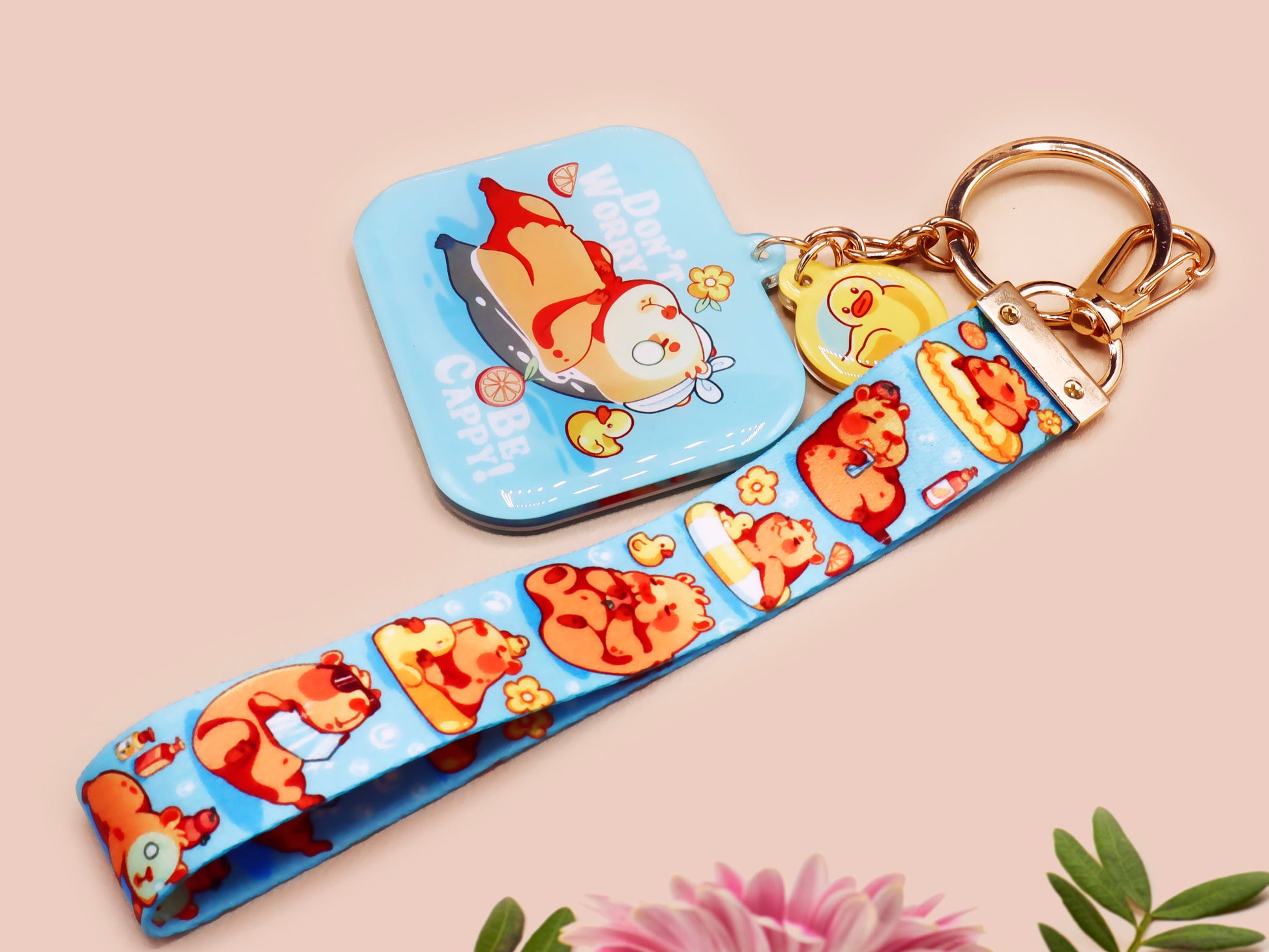 Acrylic epoxy blue capybara spa keychain with a large acrylic charm of a capybara floating in water relaxing with a face mask with the quote don't worry be cappy, a smaller charm of a cute rubber duck and a matching capybara spa day lanyard.