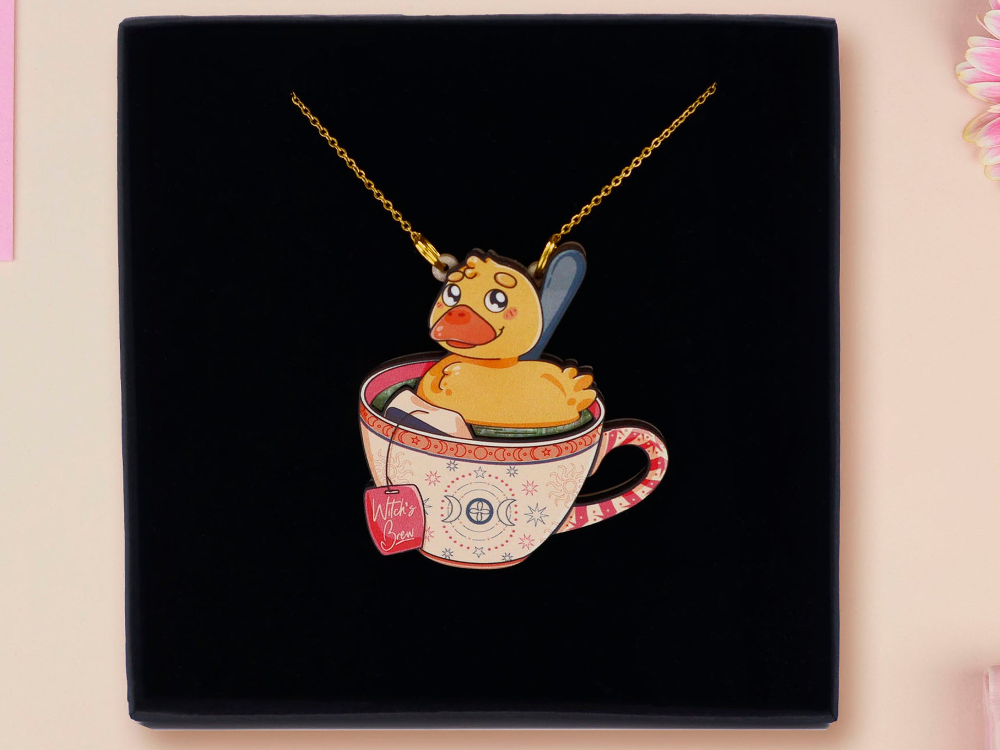 Mixed material handmade necklace of chibi cartoon duck sat in a pearlescent witch's brew teacup, with a gold chain and black gift box.