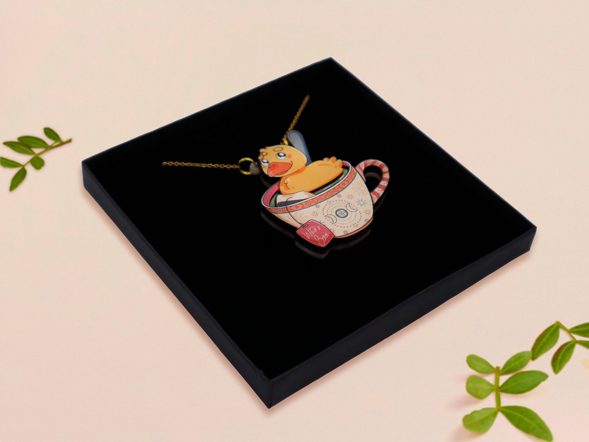 Mixed material handmade necklace of chibi cartoon duck sat in a pearlescent witch's brew teacup, with a gold chain and black gift box.