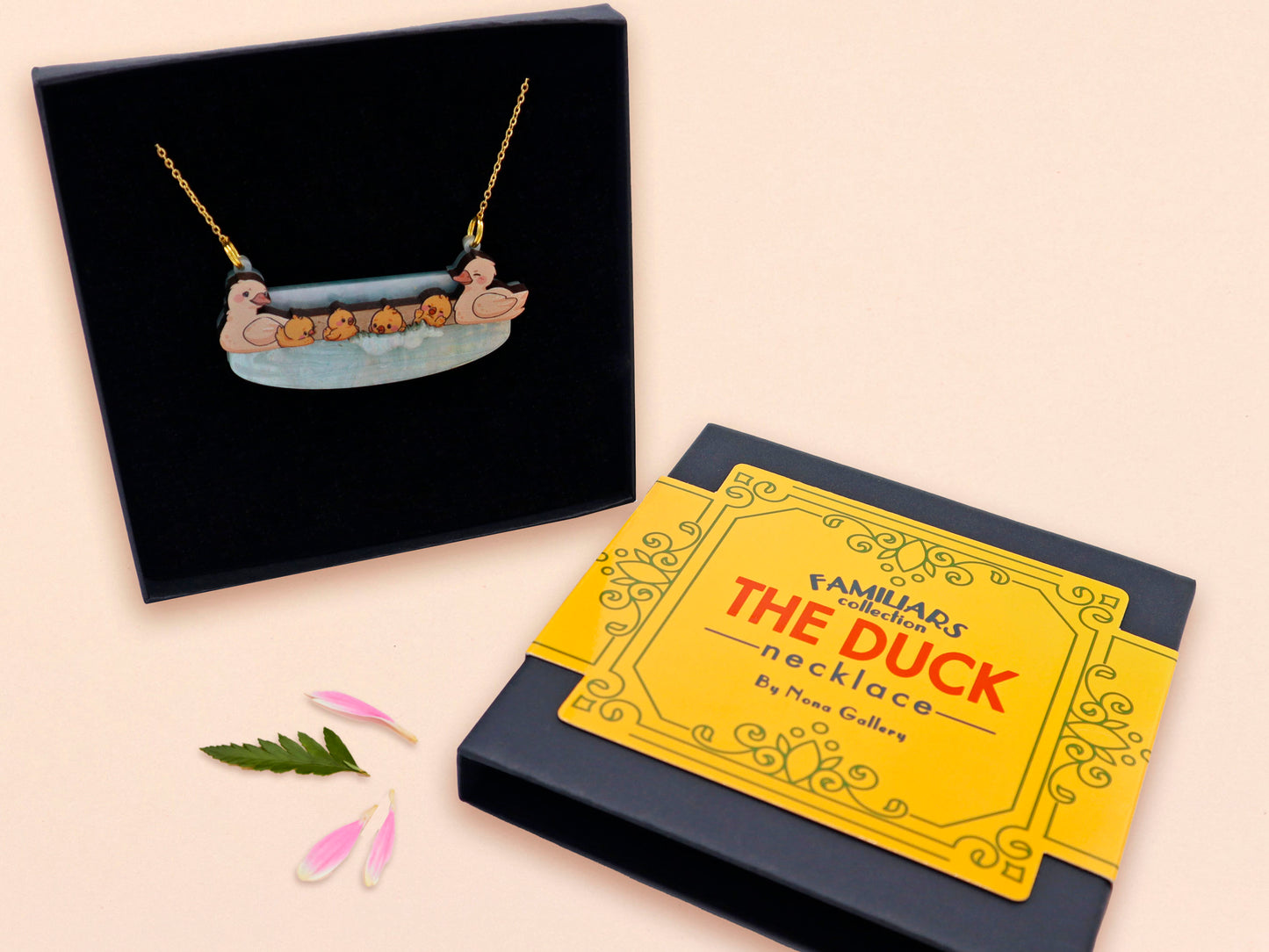 A wooden and glitter acrylic necklace with gold chain in a black box of a cute family of ducks two adult white ducks and four yellow ducklings playing and splashing in the water